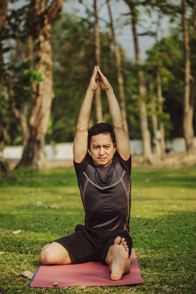 A man performing a yoga pose outdoors on a red mat, showcasing the peaceful environment of the best yoga classes near you in Kolkata.