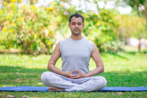 Focused young Indian man meditating in lotus pose.